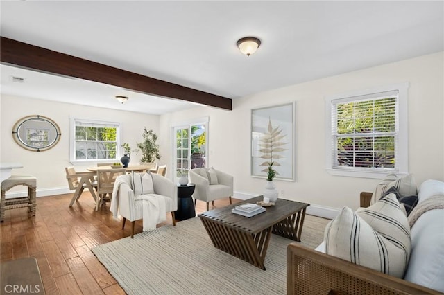 living area with visible vents, beamed ceiling, baseboards, and wood finished floors