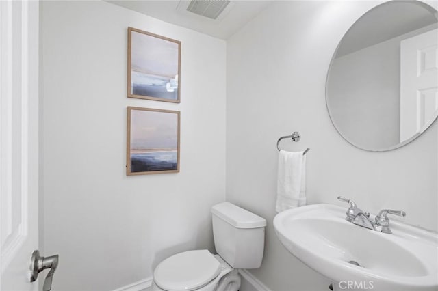 half bath featuring toilet, baseboards, visible vents, and a sink