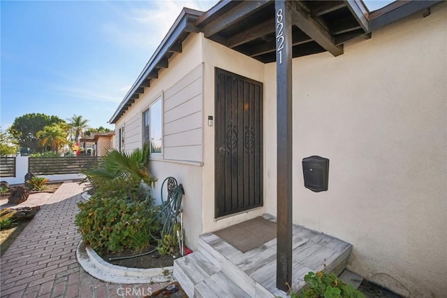 doorway to property with a patio area, fence, and stucco siding