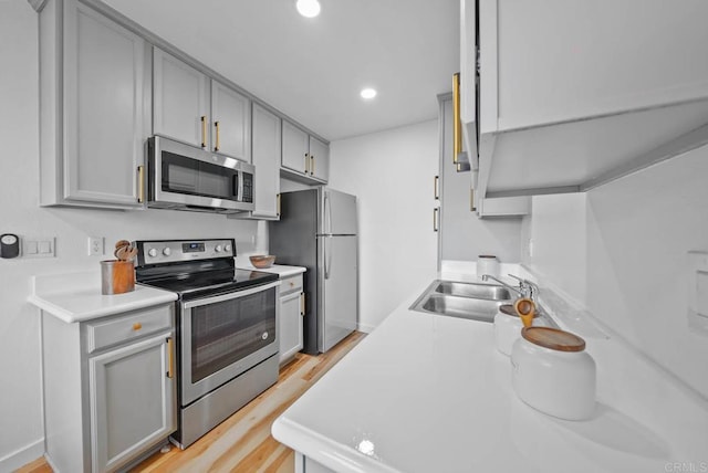 kitchen with stainless steel appliances, light countertops, a sink, and gray cabinetry