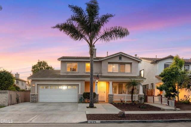 traditional home with a porch, fence, a garage, and stucco siding