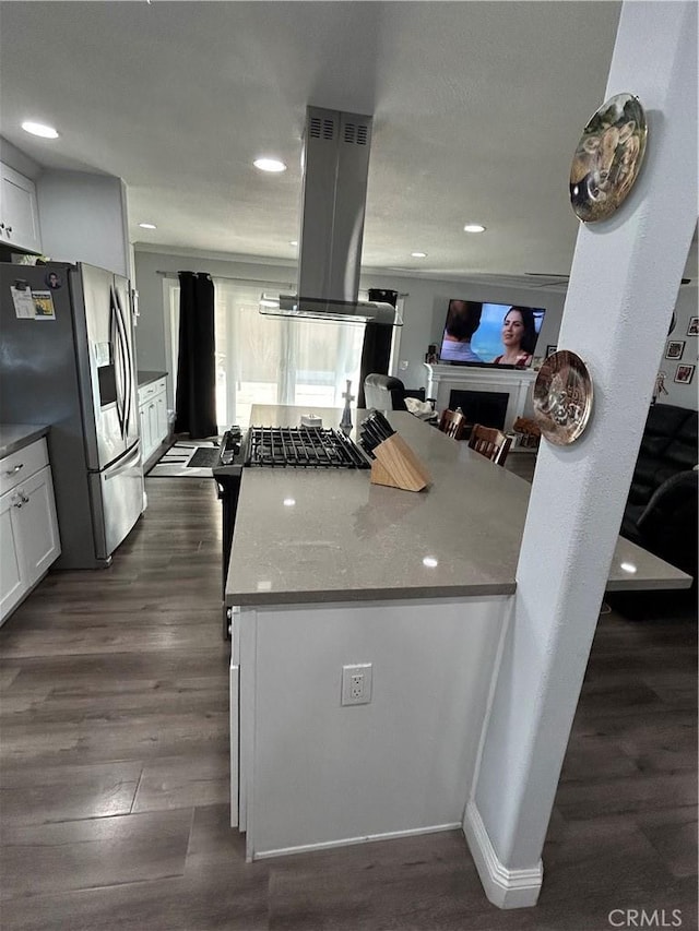 kitchen with a fireplace, stainless steel refrigerator with ice dispenser, island exhaust hood, and white cabinets