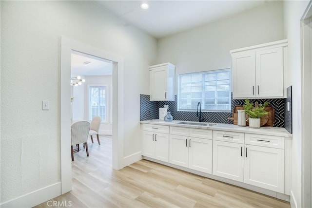 kitchen with light wood finished floors, baseboards, white cabinets, a sink, and backsplash