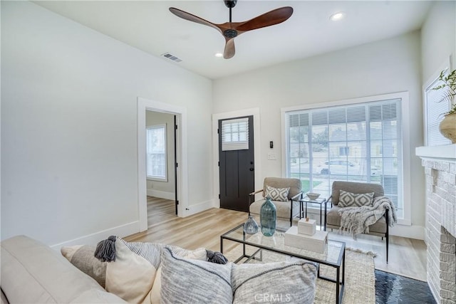 living area featuring light wood-style flooring, a fireplace, visible vents, and a ceiling fan