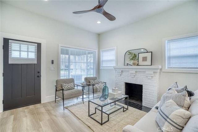 living area featuring a brick fireplace, plenty of natural light, light wood-style flooring, and ceiling fan