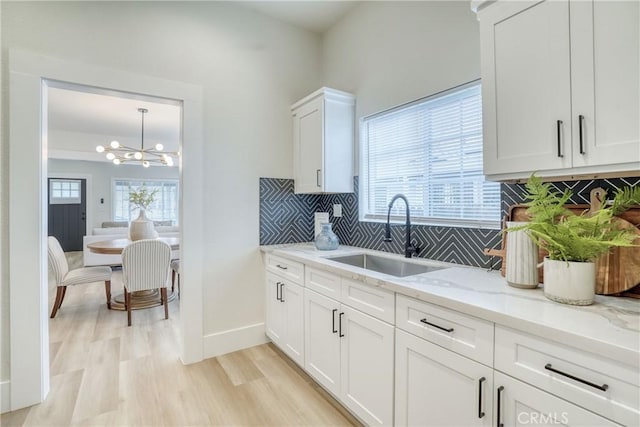 kitchen with a wealth of natural light, light stone counters, white cabinets, and a sink