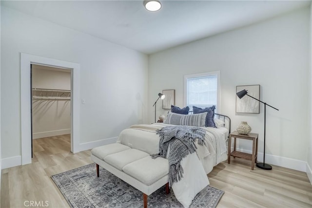 bedroom with light wood finished floors, a walk in closet, and baseboards