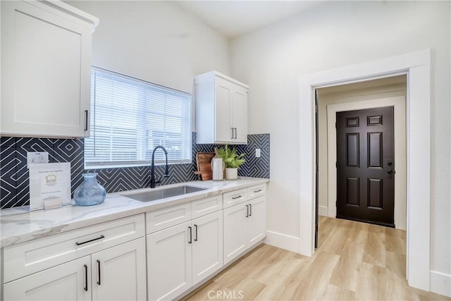 kitchen featuring light wood finished floors, decorative backsplash, white cabinets, light stone counters, and a sink