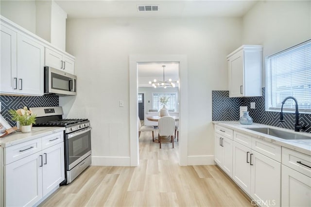 kitchen featuring a sink, visible vents, white cabinetry, appliances with stainless steel finishes, and light stone countertops