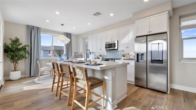 kitchen with white cabinetry, hanging light fixtures, appliances with stainless steel finishes, light countertops, and an island with sink