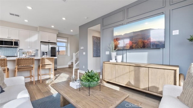 living room featuring light wood-style flooring, recessed lighting, visible vents, baseboards, and stairs