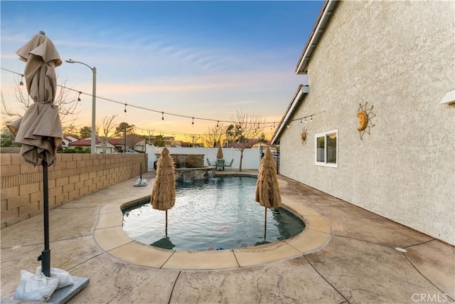 pool at dusk with a pool with connected hot tub and a fenced backyard