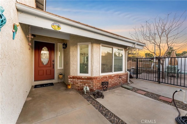 doorway to property featuring a patio area, brick siding, fence, and stucco siding