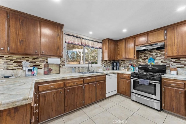 kitchen featuring stainless steel gas stove, a sink, white dishwasher, light tile patterned flooring, and under cabinet range hood