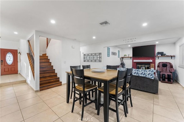 dining space featuring light tile patterned floors, recessed lighting, visible vents, a brick fireplace, and stairs