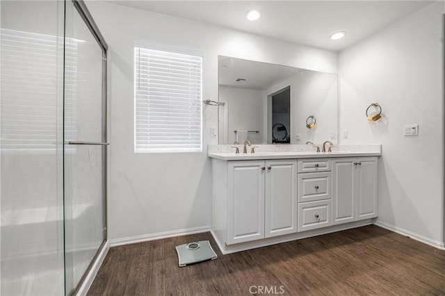 full bathroom featuring double vanity, baseboards, a shower with door, wood finished floors, and a sink