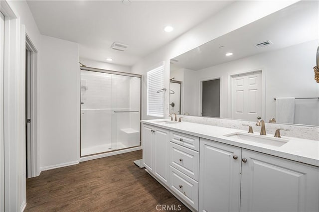 full bathroom featuring double vanity, visible vents, wood finished floors, a shower stall, and a sink