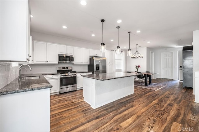 kitchen featuring stainless steel appliances, hanging light fixtures, white cabinetry, a kitchen island, and a sink