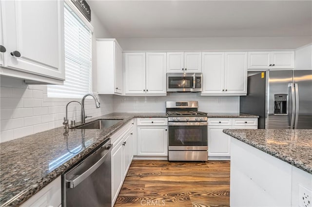 kitchen featuring white cabinets, dark stone counters, stainless steel appliances, and a sink