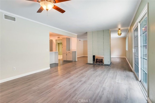 unfurnished living room featuring baseboards, wood finished floors, ceiling fan, a brick fireplace, and ornamental molding