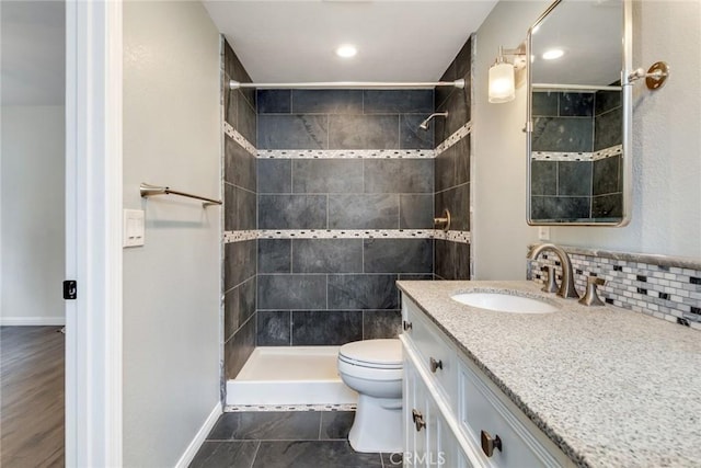 bathroom featuring toilet, a shower stall, vanity, baseboards, and decorative backsplash