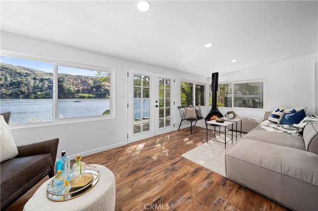 living area with recessed lighting, a water view, wood finished floors, french doors, and a wood stove