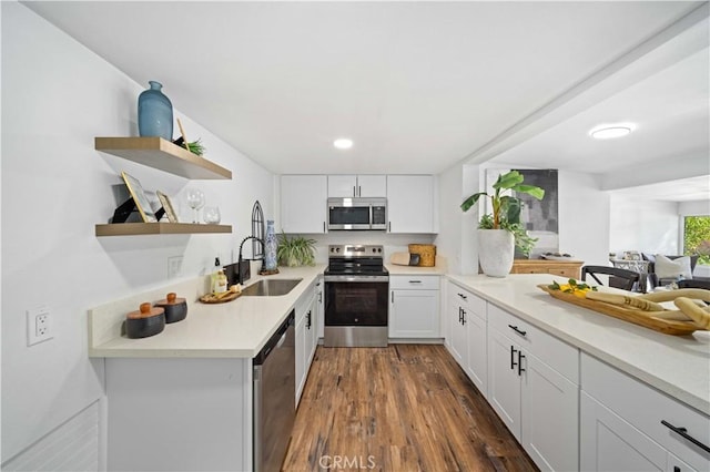 kitchen featuring dark wood-style flooring, stainless steel appliances, light countertops, white cabinets, and a sink