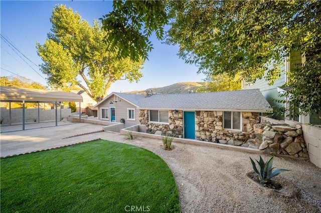 view of front of property with a shingled roof, a front yard, stone siding, and fence