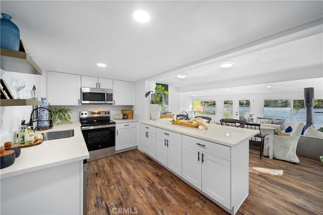 kitchen featuring stainless steel appliances, light countertops, open floor plan, white cabinets, and a peninsula