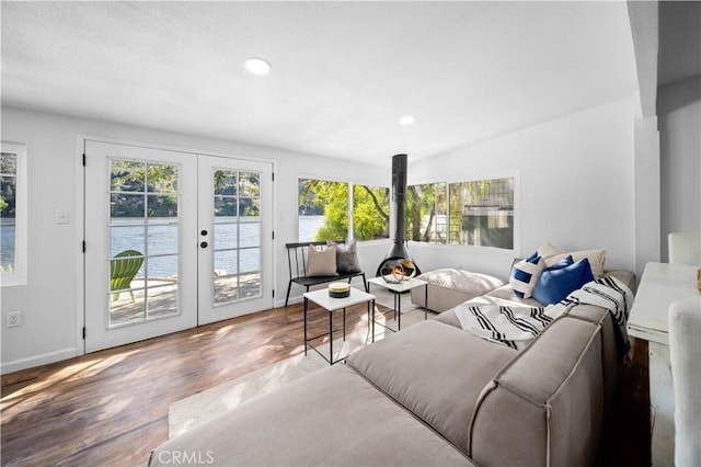 living area with recessed lighting, a water view, wood finished floors, baseboards, and french doors