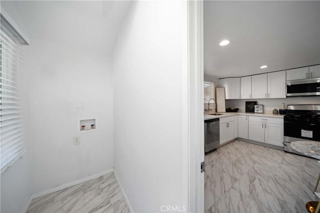 kitchen featuring marble finish floor, stainless steel appliances, light countertops, white cabinetry, and a sink