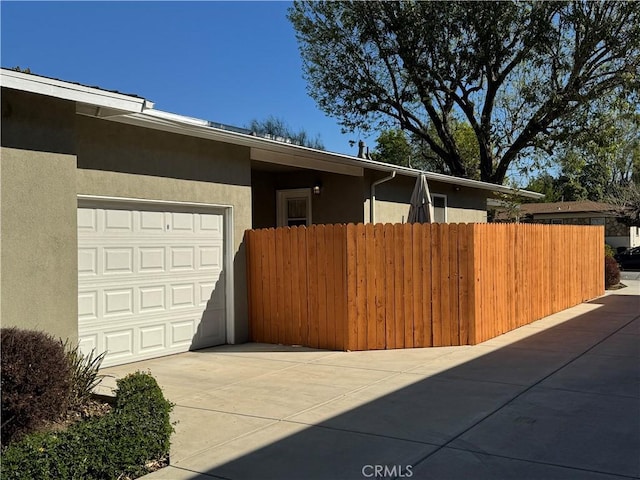 view of front of house featuring a garage, fence, driveway, and stucco siding