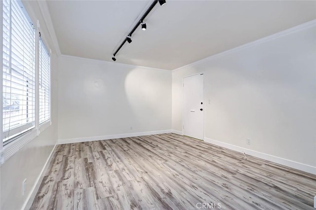 spare room featuring rail lighting, crown molding, light wood-style flooring, and baseboards