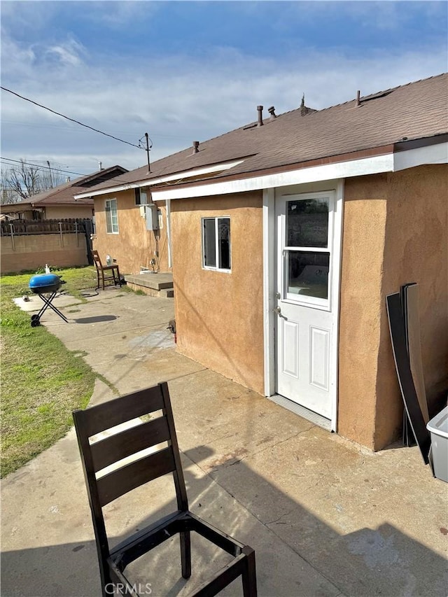 exterior space featuring a shingled roof, a patio area, fence, and stucco siding