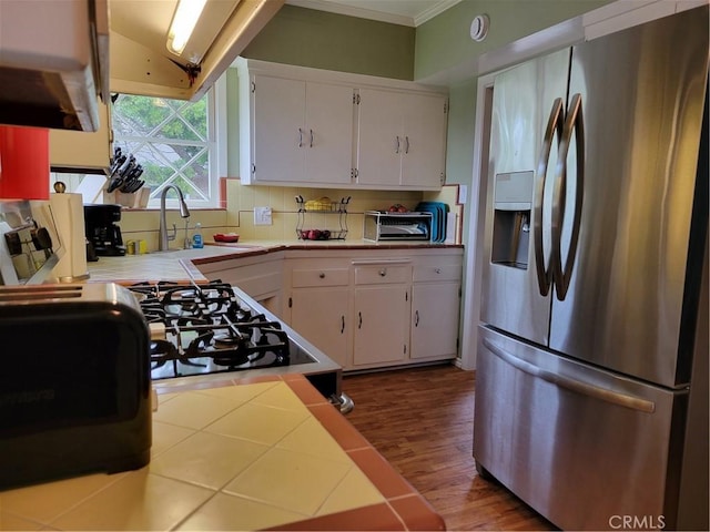 kitchen featuring a sink, white cabinets, stainless steel refrigerator with ice dispenser, backsplash, and tile counters