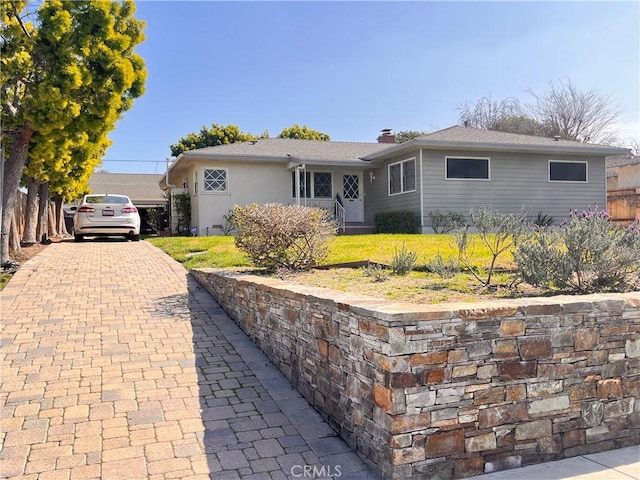 ranch-style home featuring a chimney, decorative driveway, and a front yard