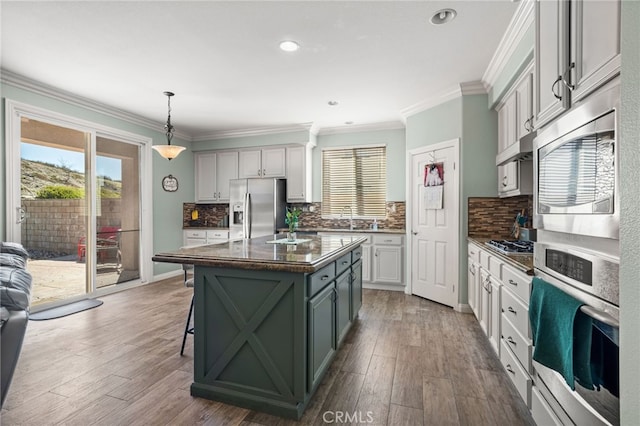 kitchen featuring a kitchen island, wood finished floors, stainless steel appliances, crown molding, and pendant lighting