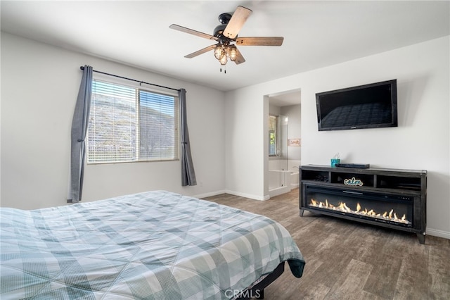 bedroom with ceiling fan, baseboards, wood finished floors, and a glass covered fireplace