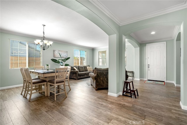 dining area featuring baseboards, arched walkways, wood finished floors, and ornamental molding