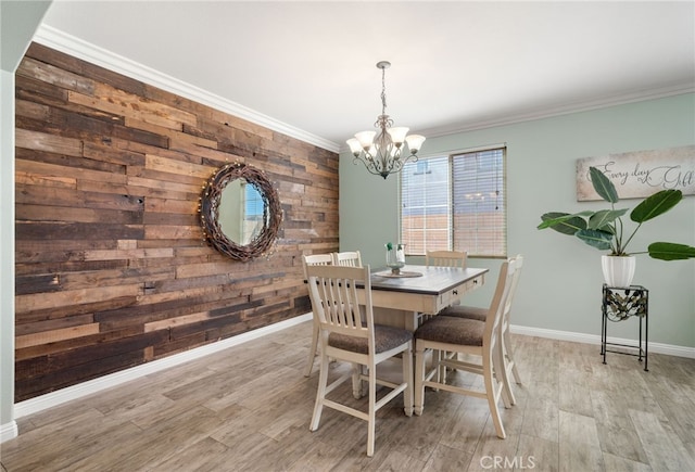 dining area with light wood-style flooring, an accent wall, ornamental molding, and a chandelier