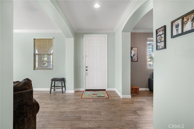 foyer with arched walkways, crown molding, light wood-style flooring, and baseboards