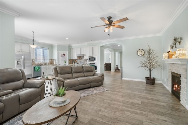 living room featuring baseboards, arched walkways, ornamental molding, and a stone fireplace