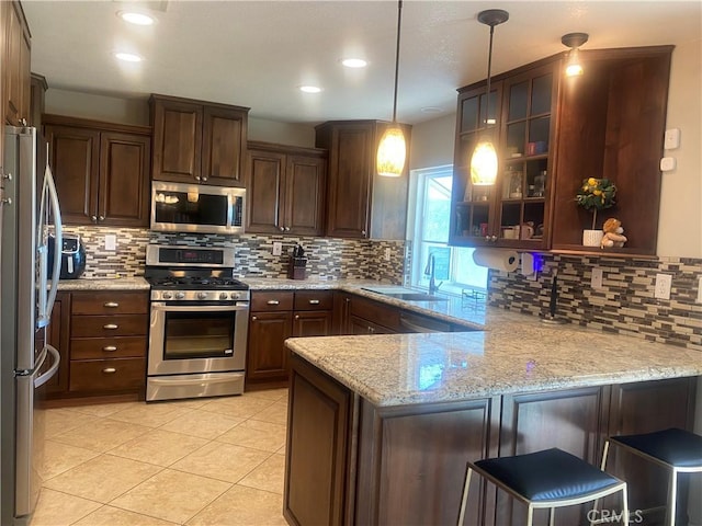 kitchen featuring a breakfast bar area, stainless steel appliances, a peninsula, glass insert cabinets, and pendant lighting