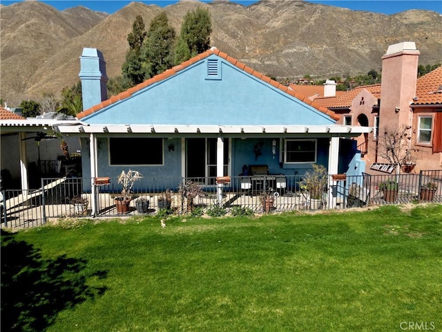 back of property featuring a yard, a mountain view, a chimney, and fence