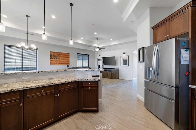 kitchen featuring light stone counters, light wood-type flooring, stainless steel fridge, a raised ceiling, and decorative light fixtures