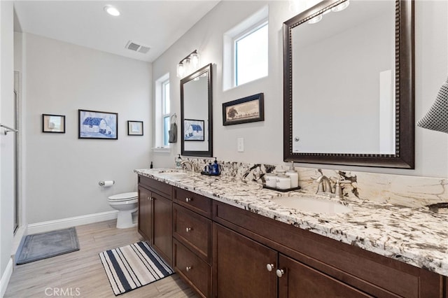 bathroom with double vanity, a sink, toilet, and baseboards