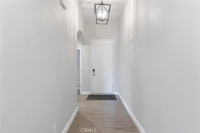 doorway with baseboards, arched walkways, wood finished floors, and a chandelier