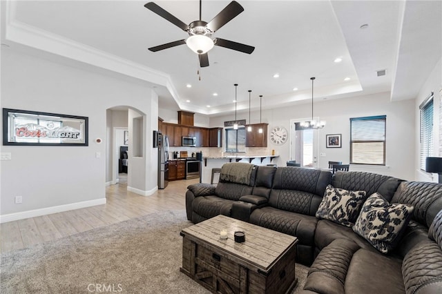 living room with arched walkways, visible vents, baseboards, light wood finished floors, and a tray ceiling