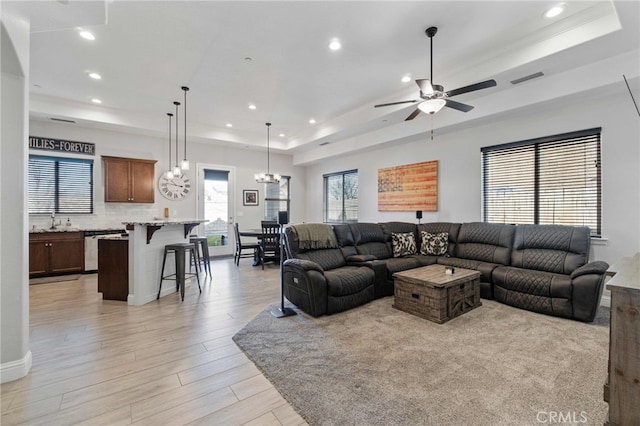 living room with light wood-style floors, a tray ceiling, visible vents, and recessed lighting