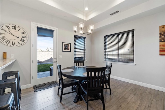 dining space featuring a healthy amount of sunlight, a notable chandelier, visible vents, and wood finished floors